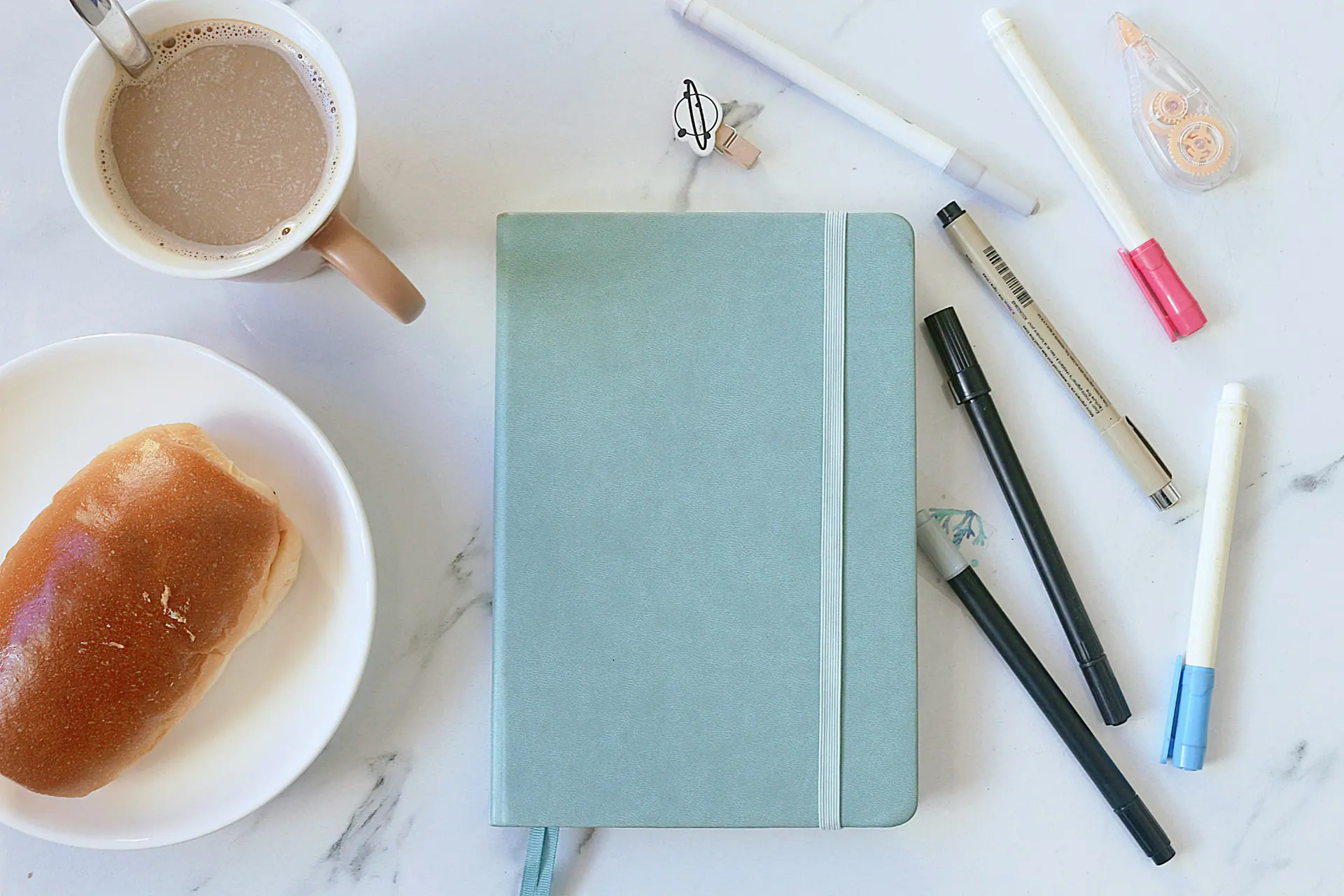 Pale blue notebook, coffee and pens arranged on a marble surface
