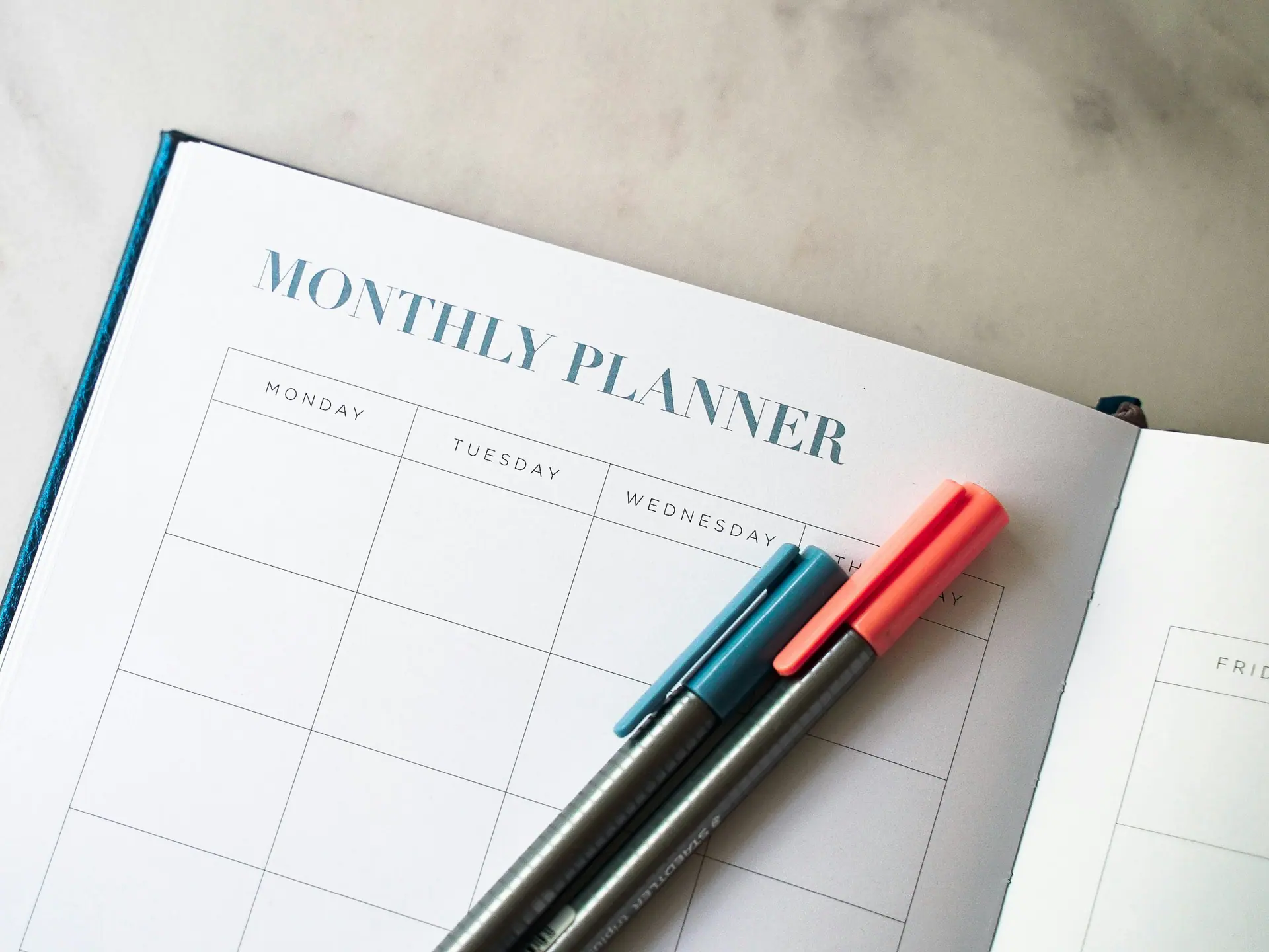 Monthly planner open on a desk beside a row of coloured pens